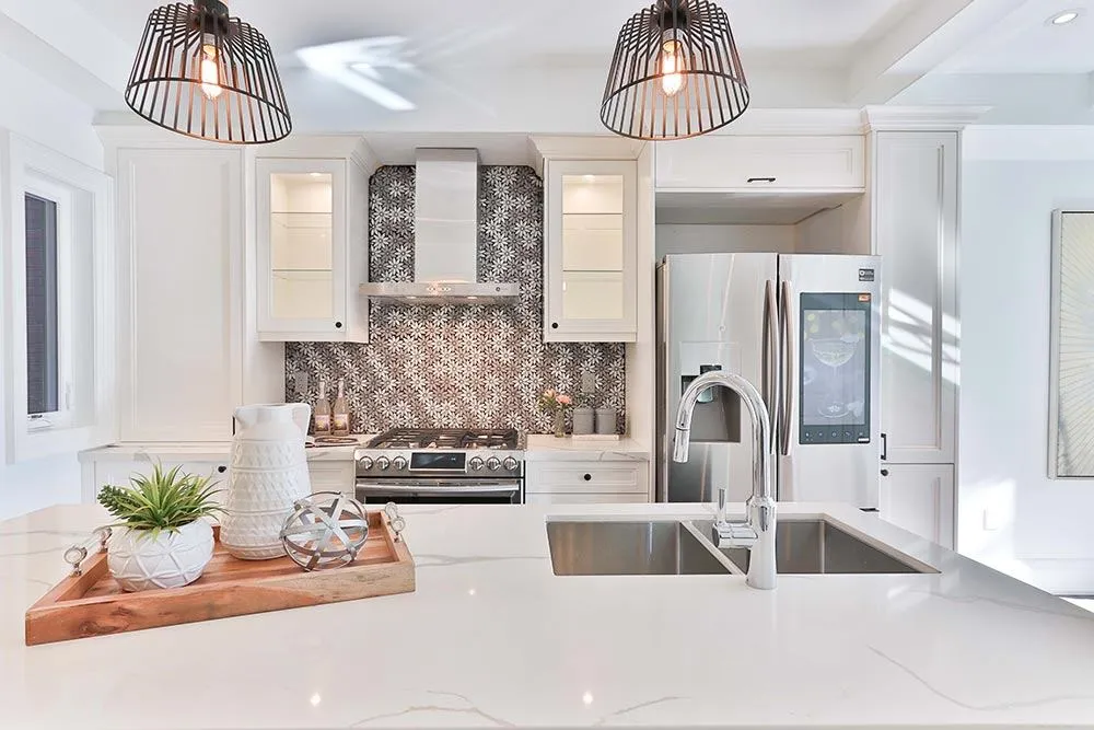 A bright, modern home kitchen with a white quartz island, stainless steel appliances, and decorative pendant lighting.