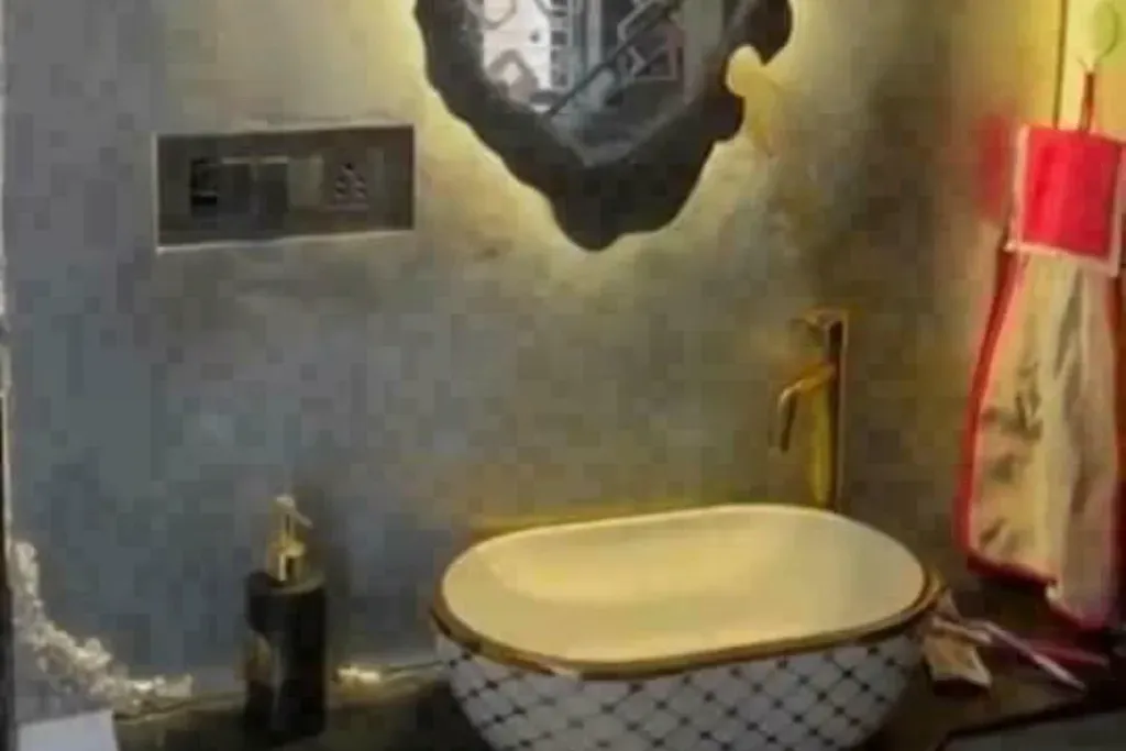 A stylish bathroom vanity with a patterned vessel sink, gold faucet, and a backlit organic-shaped mirror against a textured grey wall.