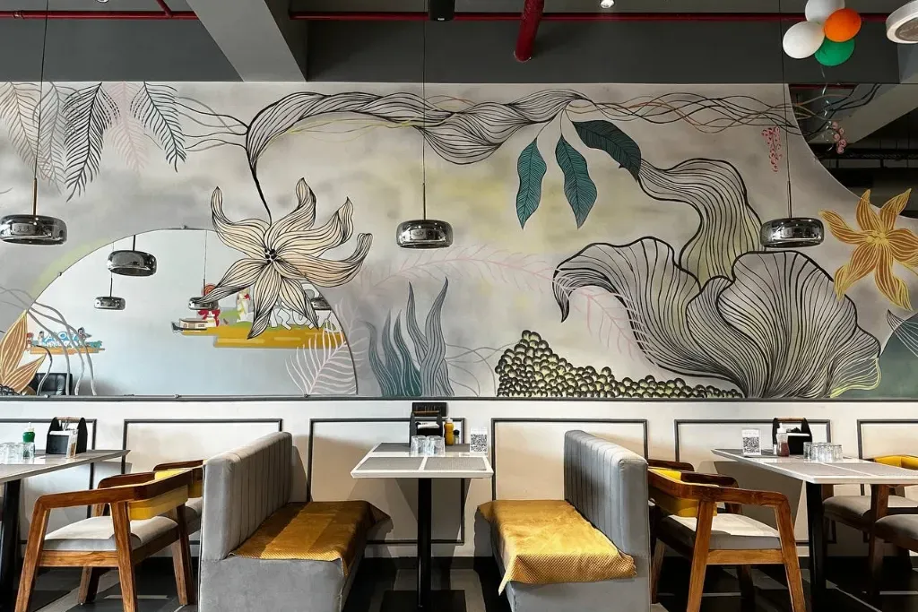 Restaurant interior remodel featuring custom booth seating, minimalist pendant lighting, and a large hand-painted botanical wall mural with large floral and leaf line art.