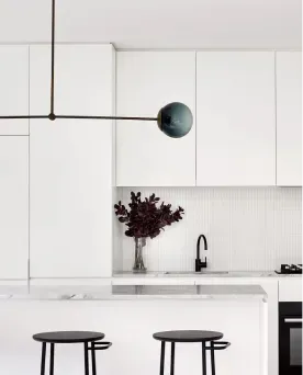 Minimalist white kitchen remodel with marble island, black stools, and modern pendant light